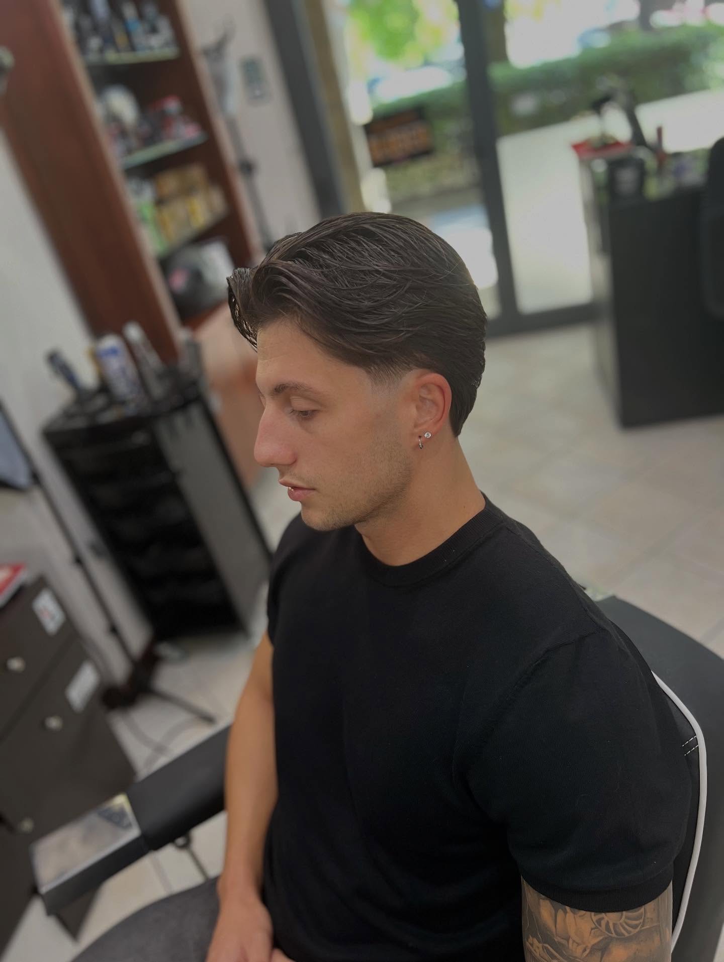 Taglio uomo con capelli pettinati indietro e sfumatura laterale