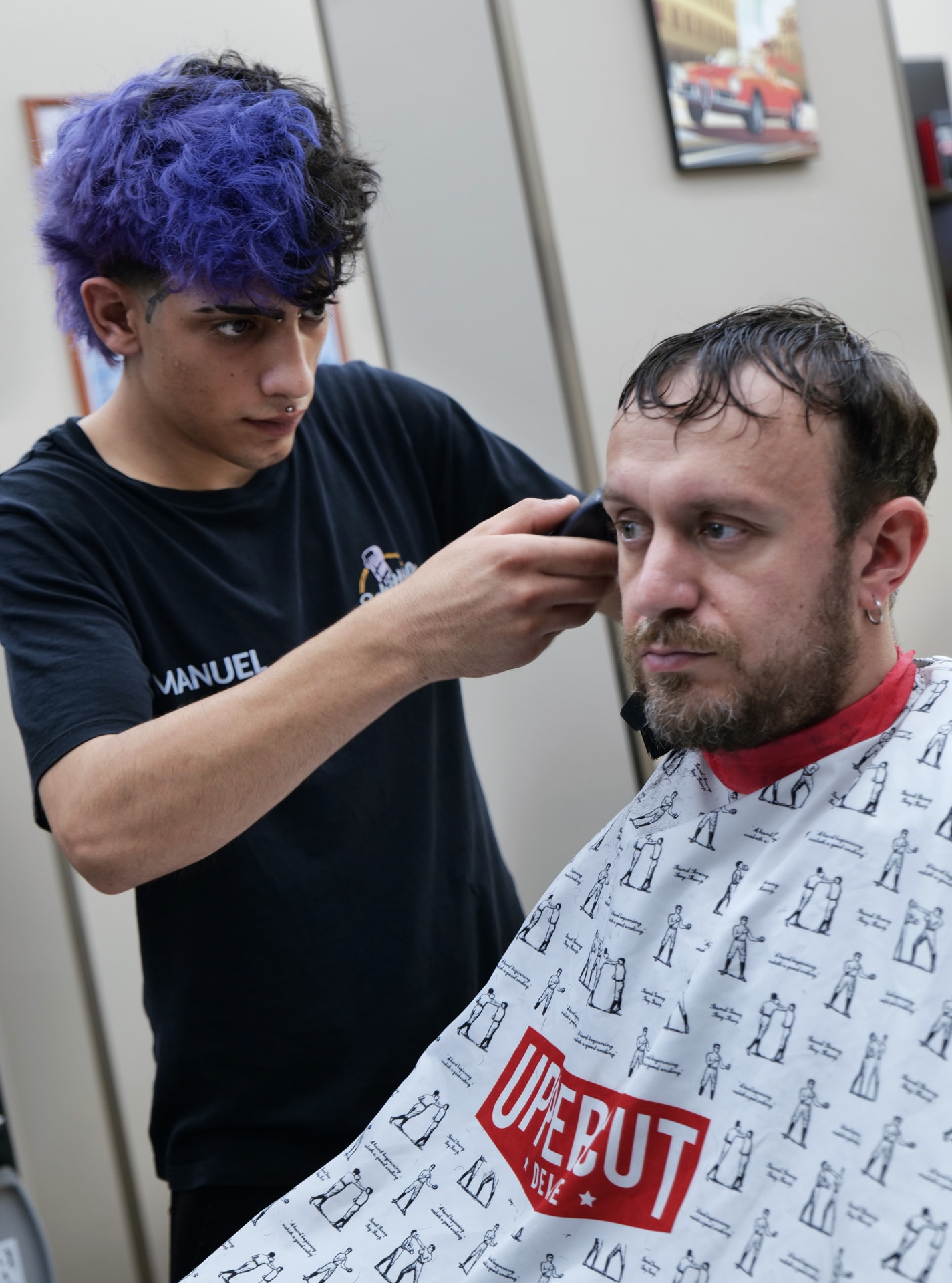 Manuel rifinisce con il rasoio il contorno di un cliente nel salone di Collegno